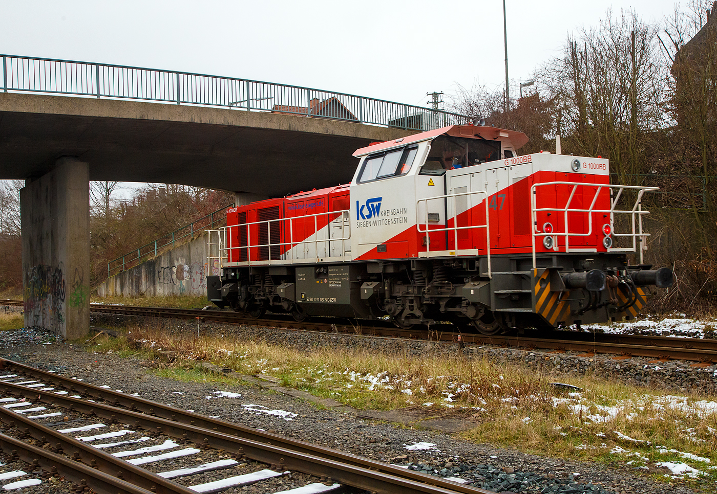 Güterverkehr gibt es noch in Herdorf....
Die KSW 47 (92 80 1271 027-5 D-KSW), ex D 2 der HFM, eine Vossloh G 1000 BB der KSW (Kreisbahn Siegen-Wittgenstein), fährt am 24.01.2023 von Herdorf auf der Hellertalbahn (KBS 462 / Strecke-Nr. 2651) in Richtung Haiger los.

Normalerweise würde sie in Richtung Betzdorf fahren, aber der Streckenanschnitt Herdorf – Betzdorf ist bis min. Ende April gesperrt, so muss die KSW den Umweg über Haiger fahren. Wobei hier als Lokzug ist es nur der Umweg und der entsprechende Mehrverbrauch an Kraftstoff, aber für den Güterverkehr ist noch die Streckenklasse sehr entscheidend und die beträgt bei dem Streckenanschnitt Herdorf – Haiger nur CE (anstatt D4 zwischen Betzdorf und Herdorf). Bei CE beträgt die Radsatzlast max. 20 t bei D4 aber 22,5 t. Dadurch kann ein Coil weniger geladen werden, da man nicht gerademal Coils vierteln kann, ergibt sich daraus ein bis zu 35% geringeres Ladegewicht und ein Mehraufwendung von Waggons.
