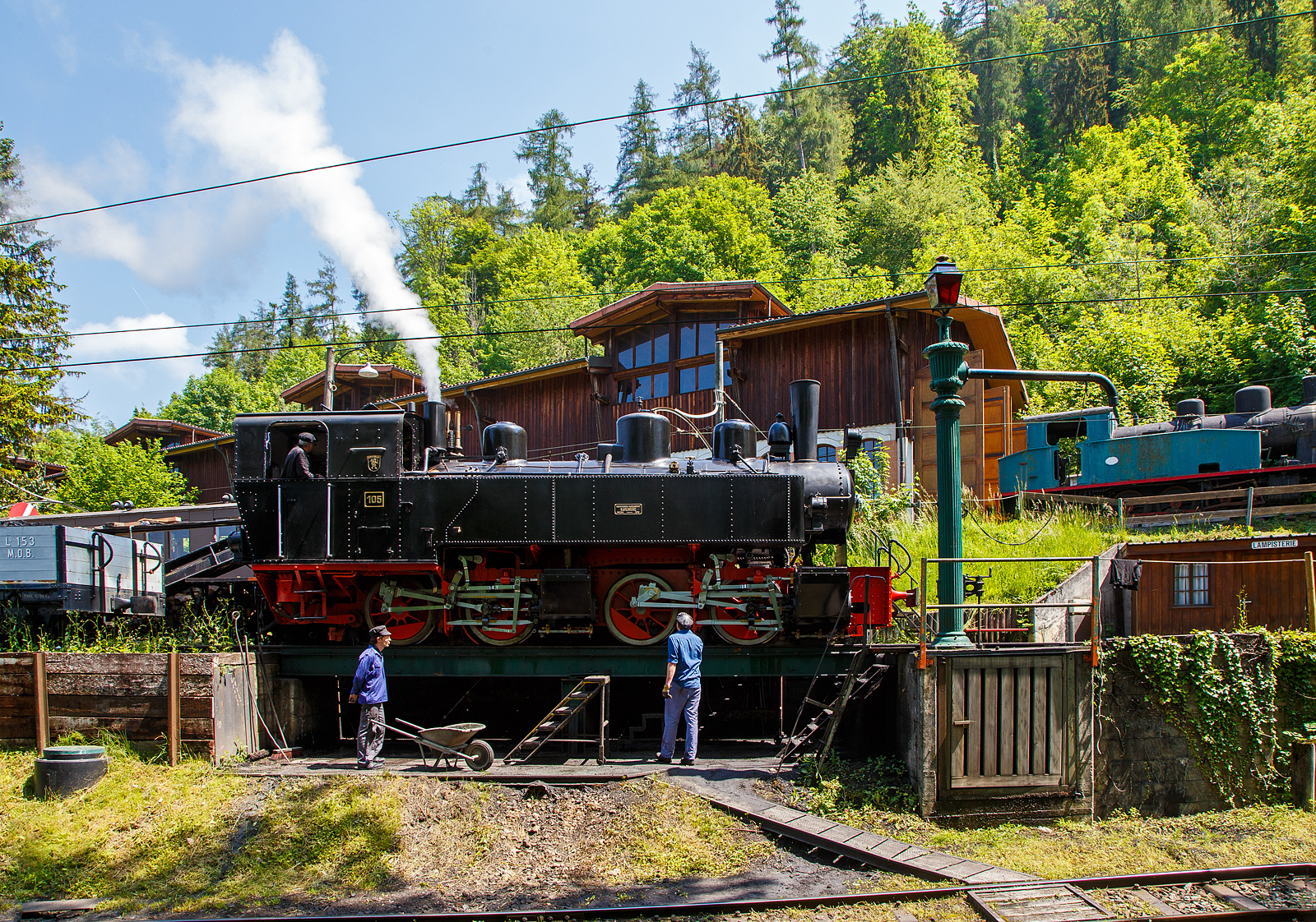 Museumsbahn-Romantik pur – Pfingsten 2023 (Samstag 27. bis Montag 29. Mai 2023) fand bei der Museumsbahn Blonay–Chamby das Schweizer Dampffestival 2023 / Festival suisse de la Vapeur 2023 statt.

Bei der Dampflok-Wartungsstelle der Museumsbahn Blonay–Chamby beim Museumsareal in Chaulin steht am 27. Mai 2023 die G 2x2/2 Mallet-Dampflok 105  Todtnau  der Museumsbahn Blonay–Chamby, ex SEG 105  Todtnau .  Links die Strecke hinab nach Blonay, rechts das Stichgleis zum Museum bzw. Depot.

Für den Einsatz auf den Meterspur-Strecken in Frankreich bestellten die Deutschen Heeresfeldbahnen bei der Maschinenbau-Gesellschaft Karlsruhe sieben Mallet-Dampflokomotiven. Aus Zeitgründen wurde keine zeitgemäße neue Serie entwickelt. Man nahm alte Konstruktionsunterlagen als Grundlage. Die Auslieferung erfolgte im August 1918. Bevor die Maschinen HK 94 bis HK 100 (HK = Heeresprüfkommission für Feldbahnen) ihren Einsatzort erreichten, war der I. Weltkrieg (Waffenstillstand von Compiegné am 11. November 1918) jedoch schon beendet. Da sie nicht mehr von den Heeresfeldbahnen benötigt und nicht zum Reparationsgut zugeordnet wurden, übernahm sie das Reichsverwaltungsamt. Dieses verkaufte in den Jahren 1919/1920 die Loks.

Die Lok wurde 1918 von der Maschinenbau-Gesellschaft Karlsruhe unter der Fabriknummer 2051gebaut und von der Heeresprüfkommission für Schmalspurbahnen abgenommen als Lok „HK 95“ abgenommen, wegen dem Kriegsende kam sie auf den Heeresfeldbahnen nicht mehr zum Einsatz. So wurde sie 1919 an die Kleinbahn Voerde-Haspe–Breckerfeld als HVB 28 verkauft. Die Kleinbahn Voerde-Haspe–Breckerfeld wurde elektrifiziert, und die  Nr. 28  wurde 1925 an die Zell-Todtnau-Eisenbahn (in der Nähe von Freiburg) der Süddeutsche Eisenbahn-Gesellschaft (SEG) abgegeben, wo sie die  Nummer 105  -  Todtnau  erhielt. Sie blieb bis zur Streckenstillegung der Linie im Jahre 1968 im Schwarzwald und ging gleich drauf an die Museumsbahn Blonay – Champy.
Es ist noch eine Schwesterlok erhalten geblieben, es ist die 99 5906 der HSB.

Konstruktion:
Das hintere Triebwerk mit den Hochdruckzylindern ist fest im Blechrahmen gelagert. Das vordere Triebwerk mit den Niederdruckzylindern ist mit einem Königszapfen mit dem hinteren Triebwerk verbunden, der genietete Kessel liegt mit Gleitplatten auf ihm auf. Seitliche Blattfedern halten das Triebwerk in einer mittigen Stellung. Beide Triebwerke haben einen Innenrahmen.

Der Dampf wird erst zu den hinteren Zylindern geleitet, von dort gelangt er über flexible Leitungen in die vorderen Zylinder. Alle Zylinder verfügen über Flachschieber und außenliegende Heusinger-Steuerung mit Hängeeisen. Die Loks verfügen über eine Wurfhebel-Handbremse und eine Dampfbremse als Zusatzbremse. Je nach Bahn wurden später Saugluft- oder Druckluftbremse als Zugbremse nachgerüstet. Auf dem Kessel sitzen zwei Sanddome, einer für jedes Triebwerk.

TECHNISCHE DATEN:
Hersteller Maschinenbau-Gesellschaft Karlsruhe (MBK)
Baujahr: 1918
Betriebsgattung: K 44.9
Kurzbezeichnung: B' B n4vt
Spurweite: 1.000 mm
Kurzbezeichnung: B' B n4vt
Länge über Puffer: 9.400 mm
Höhe über SO: 3.800 mm
Achsstand im Triebwerk: 1.400 mm
Treibraddurchmesser: 1.000 mm
Leergewicht: 28,5 t
Dienstgewicht: 34,4 t
Höchstgeschwindigkeit: 30 km/h
indizierte Leistung: 200 kW (270 PS)
Anfahrzugkraft: 47,76 kN
kleinster befahrbarer Gleisbogen: 50 m
Kesselüberdruck: 12 bar
Kohlevorrat : 1,1 t
Wasservorrat: 3,6 m³
Zylinderanzahl: 4
Zylinderdurchmesser: 280 mm (HD) / 425 mm (ND)
Kolbenhub: 500 mm
Bremse: Knorrbremse m. Z., Wurfhebel-Handbremse

Geschichte der Mallet-Lokomotiven:
Der zunehmende Verkehr auf schmalspurigen Eisenbahnen erschloss Mallet ein anderes Wirkungsfeld. Diese Bahnen benötigten stärkere und damit größere Maschinen, als es die engen Kurven der Schmalspurstrecken zuließen. Die einzige Lösung schienen hier Lokomotiven mit schwenkbaren Fahrwerken zu sein. Dazu waren bereits die Bauarten von Fairlie und Meyer verbreitet, die schwenkbare Maschineneinheiten verwendeten. Die einzelnen Einheiten wurden mit Dampf über flexible Verbindungen gespeist, die sich jedoch stets als Schwachpunkt der Maschinen erwiesen. Mallet entwickelte stattdessen eine Bauart mit zwei Fahrwerken, von denen nur das vordere, unter der Rauchkammer befindliche Fahrwerk schwenkbar gelagert war, während der Kessel fest auf dem anderen Fahrwerk ruhte. Damit reduzierte sich die Zahl der flexiblen Verbindungen um die Hälfte. Der wesentliche Unterschied der Konstruktion von Mallet im Vergleich zu den Bauarten Fairlie und Meyer war aber die perfekte Anwendung eines Verbundtriebwerkes. Der Frischdampf wird zunächst zu den Hochdruckzylindern des fest gelagerten Fahrwerks geleitet und nach dem Auslass in die Niederdruckzylinder des vorderen beweglichen Fahrwerks. Die dorthin führende bewegliche Dampfleitungsverbindung war wegen des geringeren Drucks besser beherrschbar als bei reiner Frischdampf-Versorgung. Diese Bauart ließ Mallet sich 1884 patentieren.

Dampflokomotiven haben im Allgemeinen zwei Arbeitszylinder, die Mallet-Loks besitzen diese Einrichtungen doppelt, also 4 Zylinder mit zugehörigen Triebwerksgruppen. Der Abdampf der ersten ist gleichzeitig der Arbeitsdampf der zweiten Zylindergruppe.

Schweizerische Bauartbezeichnung G2 x 2/2, Deutsche Reichsbahn Baureihe 99.590

Mallet-Lokomotive B'B n4vt
- B'B = Dampflokomotive mit 2 Triebwerken, das erste davon beweglich gelagert, zu je 2 Treibachsen
- n4 = Naßdampf und 4 Zylinder
- v = Verbundwirkung zwischen den Hoch- und Niederdruck-Zylindern
- t = Brennstoff und Wasservorräte werden auf der Lokomotive mitgeführt
- (in neuerer Schreibweise wird häufig das  t  weggelassen.
- Bei Angaben ohne  t  handelt es sich dann immer um eine Tenderlok, im Gegensatz dazu  T  = Schlepptenderlok).