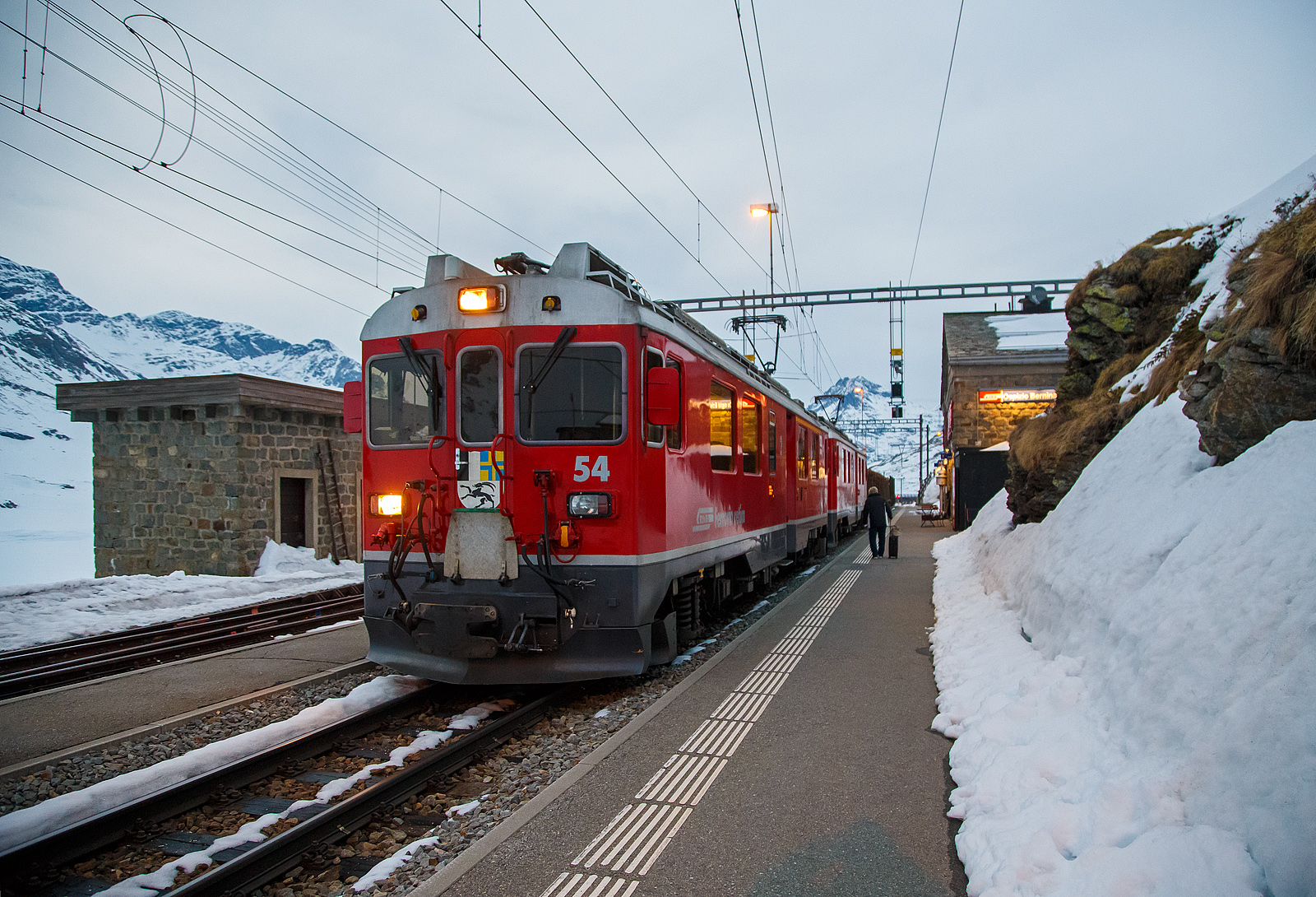 Nun haben die beiden RhB ABe 4/4 III Triebwagen 54  Hakone  und  51  Poschiavo  am 21.03.2023 als PmG (Personenzug mit Gterbefrderung) nach Poschiavo, fahren nun vom hchsten Punkt der Berninabahn, den Bahnhof Ospizio Bernina weiter nach Poschiavo.

Ab hier sind nun eher die Bremsen gefordert, denn nun geht es bis nach Poschiavo fast nur bergab. Von Pontresina nach Ospizio Bernina geht es nur bergauf, und wir merkten wie die Triebwagen arbeiten mussten.
