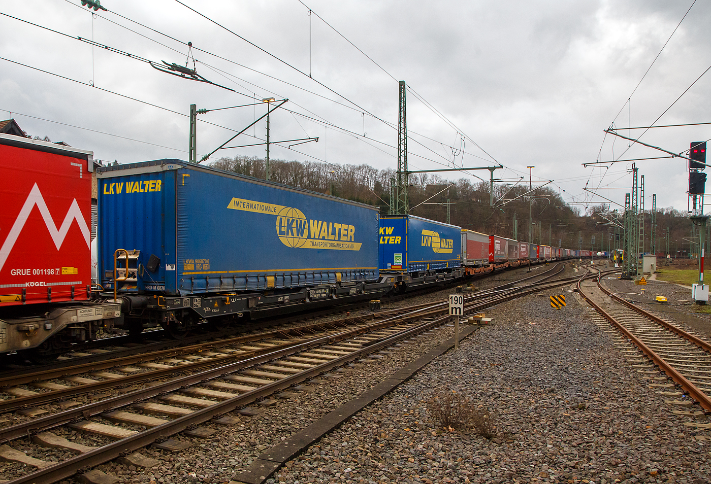 Sechsachsiger Gelenk-Taschenwagen (Doppeltaschenwagen T3000e), 37 85 4956 269-9 CH-TXL, der Gattung Sdggmrss, der TX Logistik AG (Troisdorf), am 30.01.2023 im Zugverband bei der Durchfahrt in Betzdorf (Sieg), hier beladen mit zwei Sattelanhängern von LKW Walter. Die TXL gehört seit 2017 zu 100 Prozent der Mercitalia Gruppe, einer Tochtergesellschaft der Ferrovie delle Stato Italiane. 

Diese Wagen vom Typ T3000e wurde von Tatravagónka a.s. in Poprad (Slowakei) ab 2015 gebaut, die Entwicklung und Konstruktion ist von der  Ferriere Cattaneo SA in Giubiasco (Schweiz). Baugleiche Wagen sind auch bei anderen Halteren im Einsatz, die jeweils die Gattungskennzahl 4956 haben. Mögliche Ladeeinheiten sind zwei kranmanipulierbare Sattelaufliegern oder alternativ bis zu vier Wechselbrücken und/oder Container. Dafür besitzt der Wagen einen dreifach verstellbaren Stützbock sowie für die Ladungseinheiten feste und klappbare Aufsetzzapfen auf den Langträgern. Das maximale Zuladegewicht beträgt für Sattelauflieger 2 × 40 t; die Basishöhe liegt bei 270 mm über SO.

TECHNISCHE DATEN:
Spurweite: 1.435 mm
Länge über Puffer: 34.200 mm
Drehzapfenabstand: 2 x 14.200 mm
Achsabstand in den Drehgestellen: 1.800 mm
Laufraddurchmesser: 920 mm (neu) / 860 mm (abgenutzt)
Ladelänge: 2 × 16.185 mm
Eigengewicht: 35.000 kg
Max. Zuladung bei Lastgrenze S: 100,0 t (ab Streckenklasse D)
Max. Zuladung bei Lastgrenze SS: 85,0 t (ab Streckenklasse C)
Max. Geschwindigkeit: 100 km/h (bei Lastgrenze S) / 120 km/h (bei Lastgrenze SS und leer)
Kleinster  befahrbarer Kurvenradius: R 75 m (R 150 m im Zugverband)
Intern. Verwendungsfähigkeit: TEN – GE

Ob es sich um kranmanipulierbare Sattelauflieger handelt, kann man gut an den zwei gelben Rechtecken, unten am Rahmen erkennen. Dort befinden sich die Anschlagpunkte.

Es gibt aber heute auch Systeme für nicht kranbare Sattelauflieger, wie das System NiKRASA der TX Logistik, damit werden diese kranbar und können in Taschenwagen (wie o.g.) verladen werden. Bei anderen Systemen wie LOHR, CargoBeamer oder HELROM-Trailer-Rail sind keine Krane oder Reachstacker, es sind aber besondere Systemeienge Wagen notwendig. Hervorzuheben ist hier das HELROM-System, es genügt eine asphaltierte Fläche neben dem Gleis.
