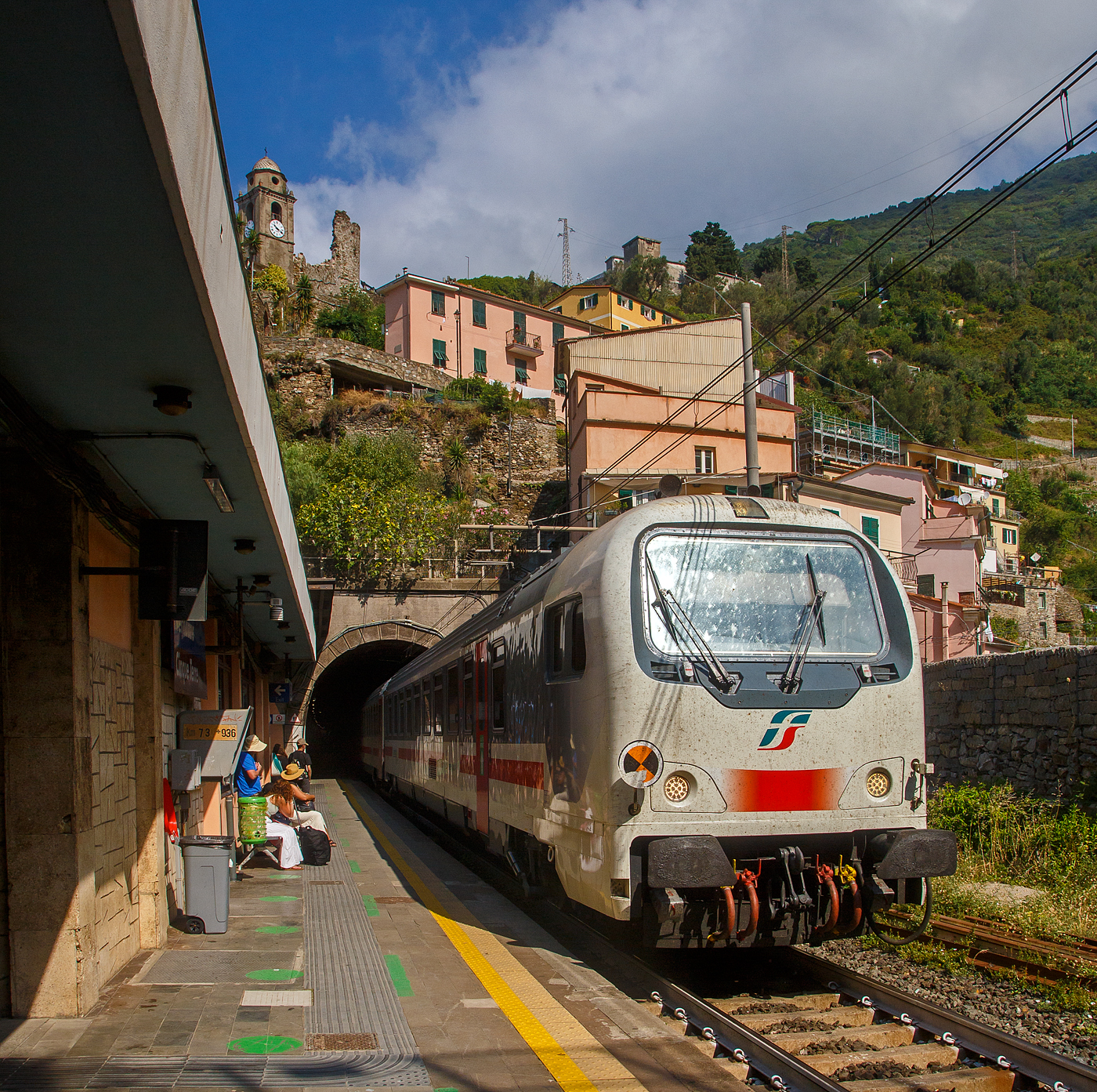 Steuerwagen voraus (geschoben von der Trenitalia E.401.011) fährt ein Trenitalia Intercity (IC) am 22.07.2022 durch den Bahnhof Vernazza (Cinque Terre) in Richtung La Spezia bzw. Pisa. 

Vernazza ist eines der fünf Dörfer der Cinque Terre (Fünf Ortschaften) und verfügt, wie die anderen Dörfer, über einen Bahnhof an der Bahnstrecke Pisa–Genua (RFI Strecke-Nr. 77 / KBS 31 La Spezia–Genua). Der Bahnhof liegt zwischen zwei zweigeteilten Tunneln, jeder Bahnsteig hat seine eigenen Tunnelröhren. Wie auch in Riomaggiore passen die Bahnsteige nicht komplett unter freien Himmel, der Rest der Bahnsteige ist jeweils in einem der Tunneln. 

Oben sieht man den Turm der Kirche San Francesco (Chiesa di San Francesco) vom gleichnamentlichen Kloster Convento di San Francesco, welches hinter der Kirche liegt.
