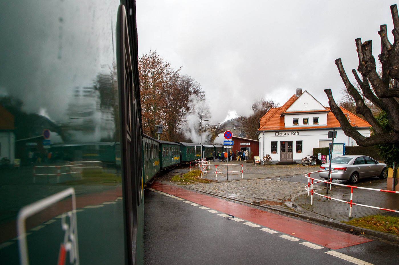 Unterwegs mit dem „Lößnitzdackel“  bzw. mit der Lößnitzgrundbahn der SDG - Sächsische Dampfeisenbahngesellschaft mbH, erreicht unser Dampfzug, gezogen von der sächsischen VII K (Altbau) 99 1761-6, nun am 07.12.2022 den Haltepunkt Weißes Roß (bei km 1,6), wir im letzten Wagen befinden uns noch am Bahnübergang Bü 1,5 - Meißner Straße in Radebeul.

Die Schmalspurbahn Radebeul Ost - Moritzburg - Radeburg ist eine sächsische Schmalspurbahn in der Spurweite von 750 mm außerhalb der sächsischen Landeshauptstadt Dresden. Für die Strecke wird heute auch die 1998 vergebene Marketingbezeichnung Lößnitzgrundbahn verwendet. Umgangssprachlich wird sie dagegen meist als Lößnitzdackel (kurz auch Dackel) oder früher Grundwurm bezeichnet.

Die in den Jahren 1911/1913 errichtete und heute denkmalgeschützte Bahnstation „Weißes Roß“ liegt nahe der Meißner Straße, wo sich die Schmalspurbahn Radebeul–Radeburg (Lößnitzgrundbahn – KBS 509) mit der Dresdner Straßenbahnlinie 4 kreuzt.

Die „Station“ besteht aus einem massiven, verputzten Bahnwärterhaus mit Fahrkartenschalter und Warteraum sowie einer nahebei gelegenen hölzernen Wartehalle. Das Bahnwärterhaus wurde 1913 durch die Königlich Sächsische Staatseisenbahnverwaltung errichtet. Es ist ein eingeschossiger, massiver Putzbau auf einem Bruchsteinsockel mit einem niedrigen Anbau, das Walmdach ist mit Ziegeln gedeckt, darin zwei Dachausbauten mit hohem Dreiecksgiebel. Die Wartehalle ist ein halboffenes, verbrettertes Fachwerk mit Pultdach.