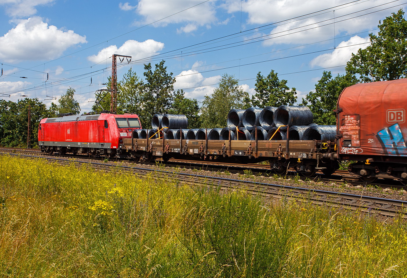 Vierachsiger Drehgestell-Flachwagen, mit Seiten-, Stirnwandklappen und Rungen, 31 80 3945 043-x D-DB, der Gattung Res 687, der DB Cargo, am 11 Juni 2024 im Zugverband bei einer Zugdurchfahrt durch Rudersdorf (Kreis Siegen) in Richtung Siegen bzw. Kreuztal. Hier beladen mit Drahtringen.

Davor die 185 062-7 (91 80 6185 062-7 D-DB) eine Bombardier TRAXX F140 AC1 der DB Cargo.