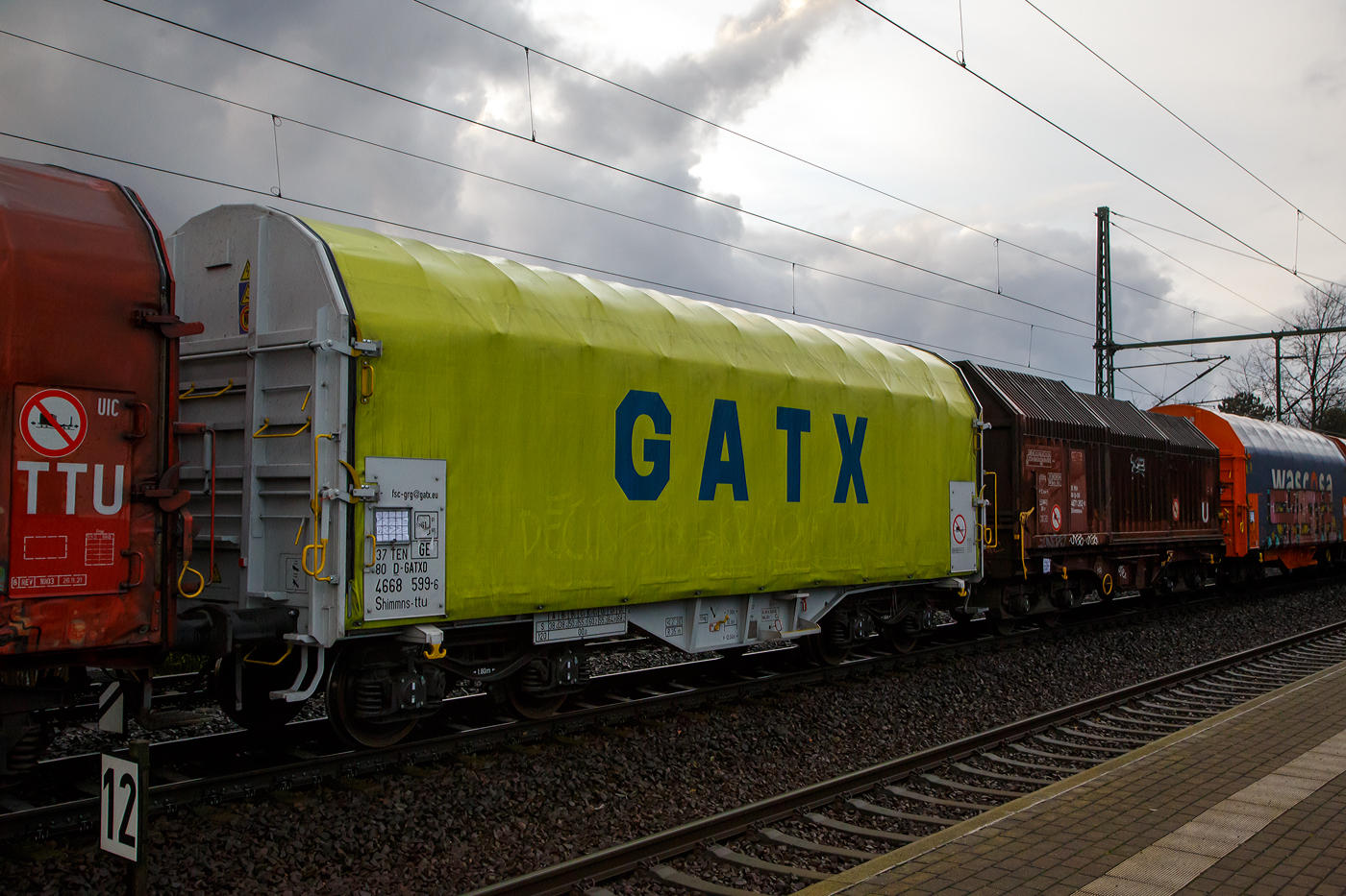 Vierachsiger Drehgestell-Flachwagen mit verschiebbarem Planenverdeck und Lademulden für Coiltransporte, 37 80 4668 599-6 D-GATED, der Gattung Shimmns-ttu, der GATX Rail Germany GmbH, am 07.12.2022 im Zugverband bei einer Zugdurchfahrt im Bahnhof Dresden-Strehlen. Der Waggonvermieter GATX (General American Transportation Corporation) ist eine US-amerikanische Leasinggesellschaft für Schienenfahrzeuge mit Sitz in Chicago. GATX wurde 1898 gegründet und ist seit 1916 an der New Yorker Börse notiert.

Diese Wagen sind speziell für den Transport witterungsempfindlicher Blechrollen (Coils) bestimmt. Er besitzt feste Stirnwände, 5 fest im Untergestell eingebaute Lademulden. Die Wagenabdeckung erfolgt mit einer PVC-beschichteten Gewebeplane, die auf 11 Rohrrahmen aufliegt. Über Laufwagen ist das Planendach in Wagenlängsrichtung verschiebbar. Die Verriegelung des Planendaches an den Stirnwänden erfolgt über eine 4-Punkt-Zentralverriegelung, die sowohl vom Erdboden als auch von der Rampe aus bedient werden kann. Das Planenverdeck lässt sich an einem Wagenende so weit zusammenschieben, dass ca. 2/3 der Ladefläche zur Beladung freigegeben wird. Hierdurch ist eine einfache Beladung des Wagens sowohl von oben als auch von der Seite aus möglich. 

TECHNISCHE DATEN:
Spurweite: 1.435 mm
Achsanzahl: 4 (in 2 Drehgestelle)
Länge über Puffer: 12.040 mm
Länge der Ladefläche: 10.800 mm
Drehzapfenabstand: 7.000 mm
Achsabstand im Drehgestell: 1.800 mm
Eigengewicht:  21.770 kg
Höchstgeschwindigkeit: 100  km/h (beladen) / 120 km/h (leer)
Maximales Ladegewicht: 68,2 t (Streckenklasse D4)
Kleinster bef. Gleisbogenradius: 35 m
Bauart der Bremse: KE-GP-A (K)
Bremssohle: C 810
Intern. Verwendungsfähigkeit: TEN - GE