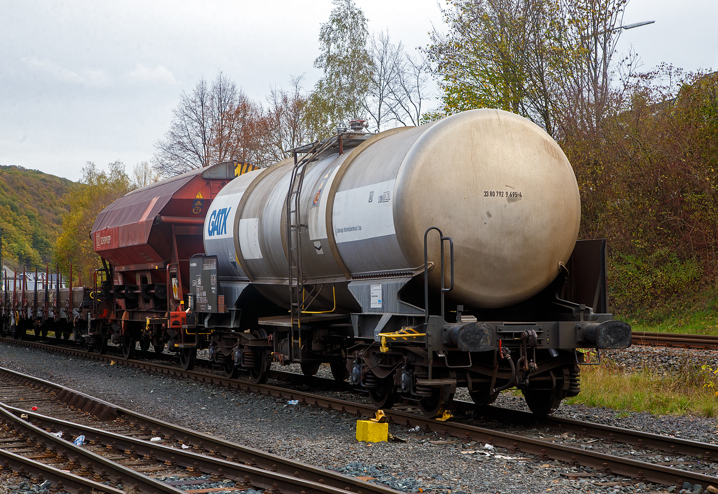 Vierachsiger-Drehgestell Kesselwagen für Salpetersäure (>97%) mit Bremserbühne, der Gattung Zacns, registriert als 33 80 7929 695-4 D-GATXD der GATX Rail Germany GmbH abgestellt, im Zugverband eines Übergabezuges der KSW, am 03.11.2022 in Herdorf auf dem Rbf. der KSW. Mieter des Wagens ist die SKW Stickstoffwerke Piesteritz GmbH (Wittenberg). 

Die Gefahrguttafel (885/2031) zeigt es auch noch an: (oben) Gefahrgutnummer 885 = stark ätzender Stoff / (unten) UN-Nummer 2031 = Salpetersäure, andere als rotrauchend, mit mehr als 70 % Säurebrandfördernd. Hier sogar (laut Anschrift) größer 97 %. Die reine Säure ist farblos und hat einen scharf stechenden Geruch. Sie wird unteranderem zur Herstellung von Sprengstoffen verwendet, was hier der Fall ist.

Der Wagen wurde 2003 vom rumänischen Wagonbauer Meva S.A. DrobetaTurnu – Severin gebaut,

TECHNISCHE DATEN:
Gattung: Zacns (Gattungszahl 7629)
Spurweite: 1.435 mm
Länge über Puffer : 12.860 mm
Drehzapfenabstand: 7.820 mm
Achsabstand im Drehgestell: 1.800 mm
Laufraddurchmesser 920 mm (neu)
Höchstgeschwindigkeit: 100 km/h
Eigengewicht: 20.250 kg
Nutzlast: 69,7 t ab Streckenklasse D3 (CM 63,7 t)
Kleinster befahrbarer Gleisbogen: R 35 m
Gesamtvolumen: 50,450 Liter
Prüfdruck: 4 bar
Zulässiger Betriebsüberdruck: 3 bar
Tankcode: L10DH
Behälterwerkstoff : Edelstahl
Intern. Verwendungsfähigkeit: RIV

Auch im dahinter befindlichen Wagen dem gedeckten Schüttgutwagen 21 80 0734 600-8 D-DB, der Gattung Tds 937, wurde ein Rohstoff für die Herstellung von Sprengstoffen transportiert und zwar Ammoniumnitrat.