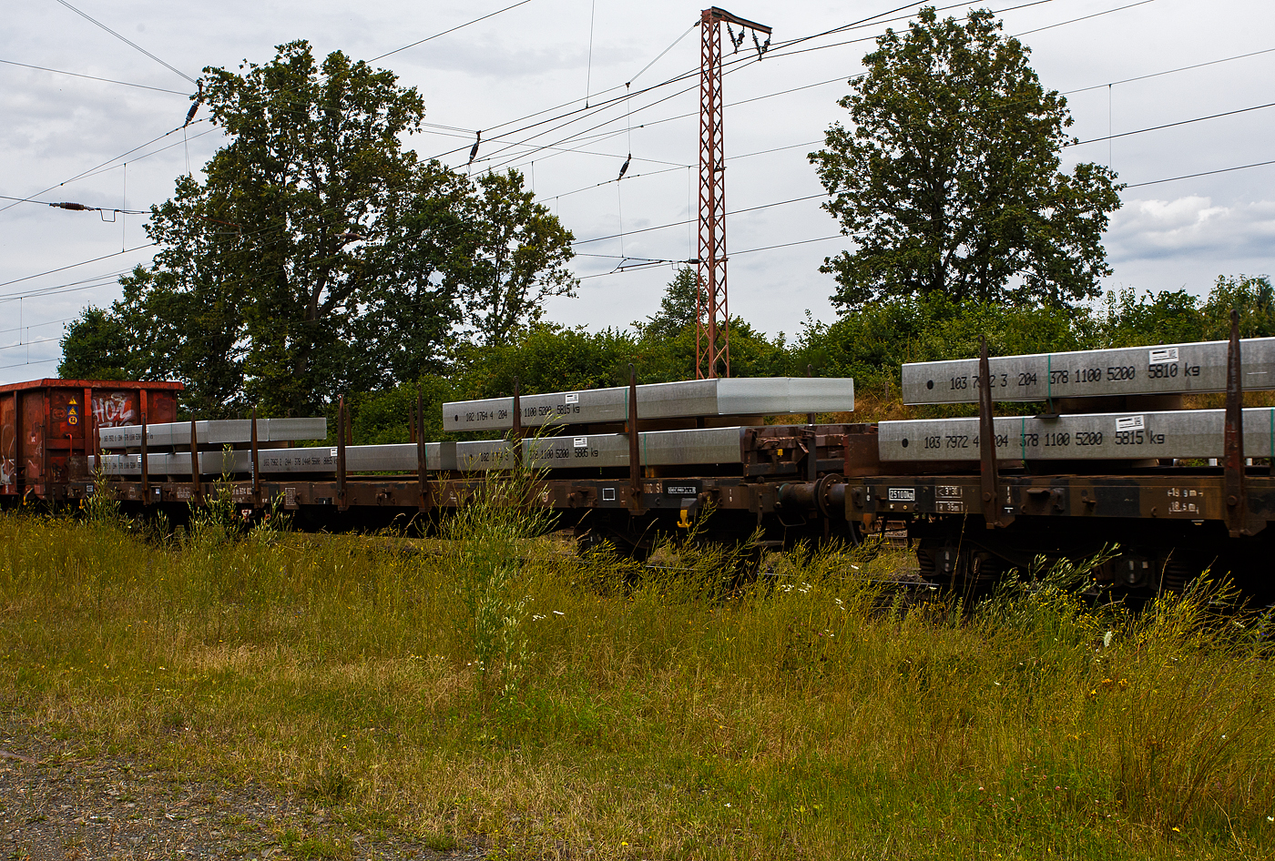 Vierachsiger Drehgestellflachwagen mit Rungen und Stirnwandklappen, jedoch ohne Seitenwandklappen (Rungenwagen), 31 80 3914 896-6  D-DB, der Gattung Rs 689, der DB Cargo AG, am 19 Juli 2024 im Zugverband bei einer Zugdurchfahrt durch Rudersdorf (Kreis Siegen). Beladen ist der Wagen hier mit 9 Aluminium-Brammen mit einem Stückgewischt von 5.600 bis 6.600 kg. So ist der Wagen gemäß Lastgrenzenraster für die Streckenklasse C gut ausgeladen (aber nicht überladen). 

Der Wagen wurde 1977 von MAN in Nürnberg gebaut.