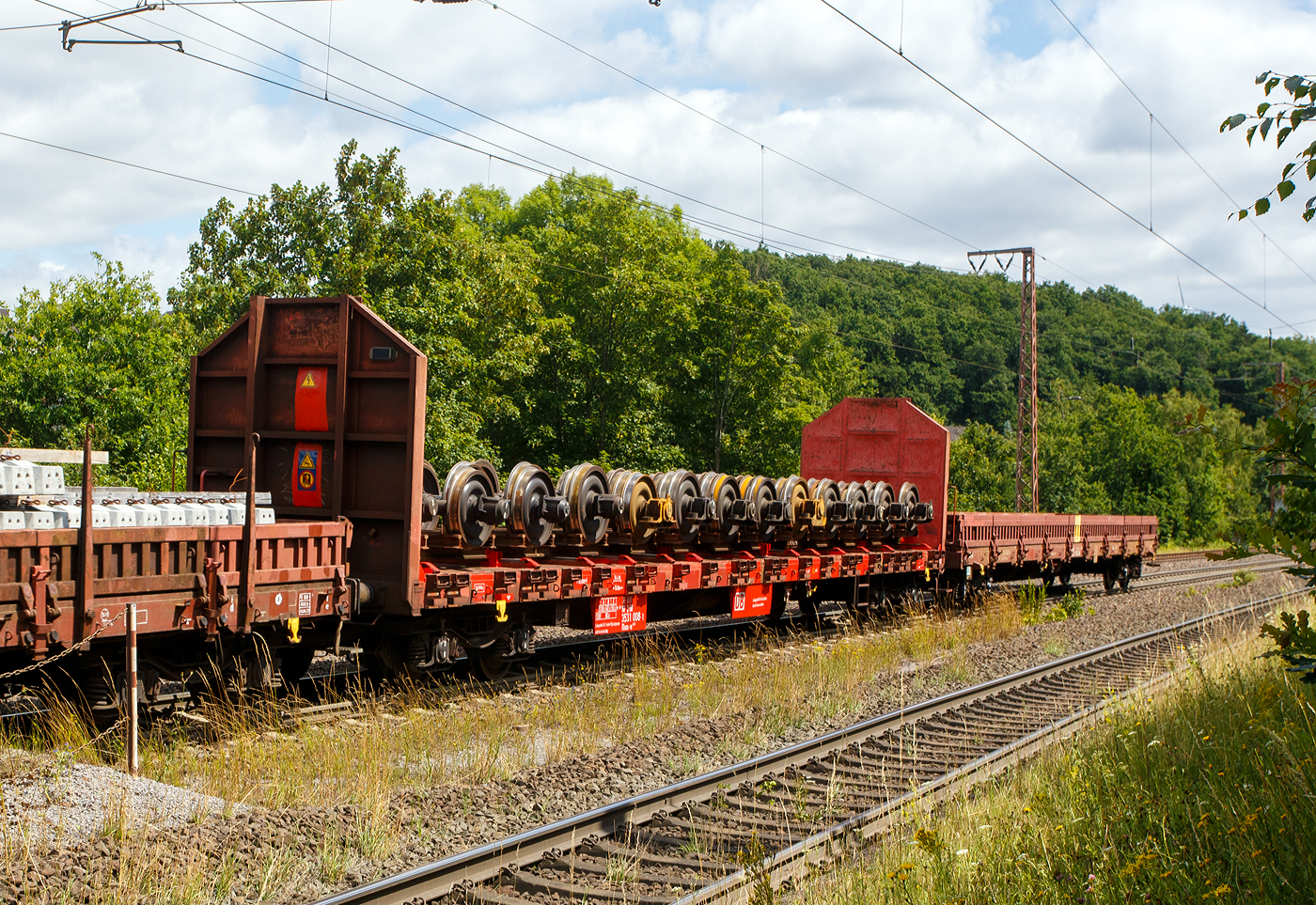 Vierachsiger Drehgestellflachwagen ohne Rungen, mit festen hohen Stirnwänden, 31 80 3531 008-1, der Gattung Rloos-w, der DB Cargo AG, am 11 Juli 2025 im Zugverband bei einer Zugdurchfahrt durch Wilnsdorf-Rudersdorf (Kreis Siegen), hier beladen mit Güterwagen-Radsätzen. Vermutlich ist es ein speziell für den Transport von Radsätzen umgebauter Wagen. 