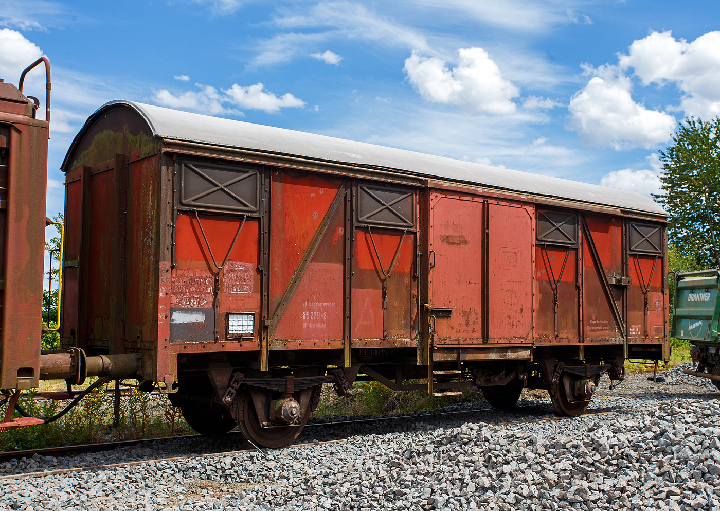 Zweiachsiger gedeckter Güterwagen als DB Bfwg 65 279-2 Bf Siershahn (DB Bahnhofswagen), ehem. zweiachsiger gedeckter Güterwagen 01 RIV-EUROP 80 DB 120 7 614-9, der Gattung Gs 210, ausgestellt am 07 Juli 2024 beim Erlebnisbahnhof Westerwald der Westerwälder Eisenbahnfreunde 44 508 e. V. in Westerburg, hier war Lokschuppenfest.

TECHNISCHE DATEN als Gs 210:
Spurweite: 1.435mm
Achsanzahl: 2
Länge über Puffer:  11.080 mm
Radsatzstand:  5.700 mm
Ladelänge:  9.280 mm
Ladebreite:  2.710 mm
Ladefläche:  25,2 m²
Laderaum:  64,0 m³
Türöffnung (B × H):  2.000 × 2.000 mm
Höchstgeschwindigkeit: 100 km/h
Kleinster bef. Gleisbogenradius:  35  m
Bauart der Bremse:  KE-GP
Austauschverfahren:  01
Intern. Verwendungsfähigkeit:  RIV-EUROP

Der Internationale Eisenbahnverband (Union internationale des chemins de fer, UIC) gründete im Jahre 1949 eine eigene Forschungs- und Entwicklungsanstalt (ORE) und legte damit den Grundstein für international gültige Baugrundsätze von Güterwagen. Auf den ausgearbeiteten Entwürfen und Grundlagen der ORE für einen zweiachsigen Standard Güterwagen, entwickelten die Europäischen Bahnverwaltungen alsbald Ihre eigenen Fahrzeuge. Diese konnten dem Grundgedanken des UIC entsprechend, innerhalb der Gebiete der Mitgliedsverwaltungen zum Transport von Waren und Gütern eingesetzt werden. Die Deutsche Bundesbahn machte mit den ersten rund 3.500 Wagen (nach den vorläufigen Entwürfen) den Anfang und konnte bereits ab 1957 mit dem Gmm(e)hs 56 die ersten 2.662 echten UIC-Standardwagen in Betrieb nehmen. Äußerlich wurde die standardisierte Bauart durch die Anschrift RIV St UIC kenntlich gemacht. Andere Bahnverwaltungen wie die SNCF, FS, ÖBB, NS, DSB, MAV, P.K.P., CFL, SBB agierten in ähnlicher Art und Weise und fertigten ihre eigenen Ausführungen der UIC-Standardwagen. Durch diesen Umstand sind sich die Wagen alle sehr ähnlich, weisen aber zudem immer wieder länderspezifische Bauartunterschiede auf. Da die DB selbst einen sehr großen Bedarf an neuen Wagen hatte und es zudem bei älteren Wagengattungen einen Modernisierungsstau gab, kam es nicht nur zum Komplettneubau von UIC St Wagen. In mehreren Umbauprogrammen, bei denen einzelne Teile älterer Wagen wiederverwendet wurden, entstanden nach und nach die Wagenbauarten Gmms 44, Gmm(eh)s 60, Gmms 40 sowie 216. Für die 1960er bis 1990er Jahre waren diese Wagenbauarten prägend für den Güterverkehr in Europa und mit über 100.000 gebauten Stück in fast jedem Güterzug eingereiht.
