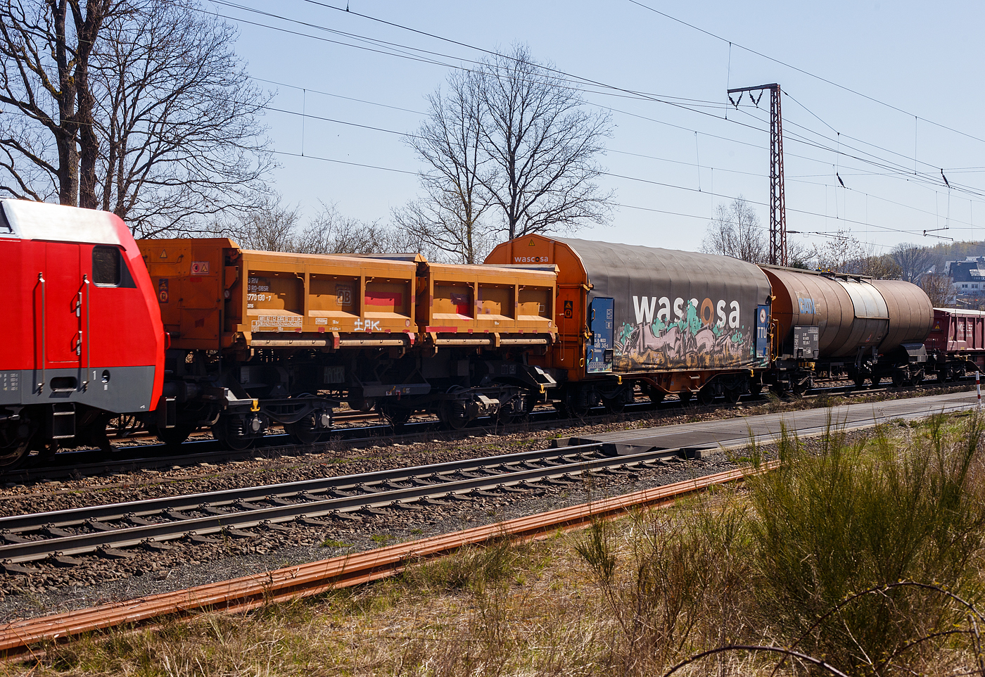 Zweimuldiger vierachsiger Drehgestell-Schüttgutkippwagen mit elektrohydraulischer Betätigung, 33 53 6770 130-7 RO-DBSR, der Gattung Fans 128, der Deutsche Bahn Cargo Romania SRL (ex DB Schenker Rail Romania SRL), am 12 April 2025 im Zugverband bei der Durchfahrt in Rudersdorf (Kr. Siegen).

Der zweimuldige Drehgestell-Schüttgutkippwagen (Zweiseiten-Kastenkipper) ist für den Transport von feuchtigkeitsunempfindlichen Schüttgütern wie z.B. Splitt, Kies, Schotter, erdfeuchtem Sand, Bodenaushub oder Bauschutt vorgesehen. Der Wagen besitzt einen elektrohydraulischen Kippantrieb und eine speicherprogrammierbare Steuerung (SPS). Entwickelt und in Serie gebaut wurde der Kastenkipper vom FEW Fahrzeug- und Entwicklungswerk Blankenburg (Harz) der DB AG. Die Drehgestelle liefert das Werk Halle, die Wagenkästen fertigen das Werk Kaiserlautern und DWA Niesky.

Für den Einsatz als Einzelwagen, in Wagengruppen oder beim Massenschüttgut-Transport in Ganzzügen besitzt er eine autarke Wagentechnik, die eine von äußeren Energiequellen unabhängige Entladung ermöglicht. Das Schüttgut kann als Nah- oder Weitablage abgegeben werden. Das Schüttgut beiden Seiten gekippt werden. Der Wagen verfügt über zwei getrennt kippbare Mulden. Die Wagen haben eine Batterie die über Achsgeneratoren (hier im Bild an der 2. Achse von rechts) aufgeladen werden.

TENISCHE DATEN:
Erstes Lieferjahr: 1996
Spurweite: 1.435 mm (Nprmalspur)
Länge über Puffer: 11.600 mm
Drehzapfenabstand: 6.580 mm
Achsabstand im Drehgestell: 1.800 mm
Drehgestell-Bauart: Y 25 Lsd 1 - 629
Laufraddurchmesser: 920 mm (neu)
Laderaum: 2 x 18,0 m³
Ladefläche: 2 × 12,0 m²
Höhe der Beladeöffnung: 3.512 mm
Kippwinkel des Kastens: 45°
Kippantrieb Energieversorgung: autark, über Batterie laden über Achsgenerator
Kippantrieb Kapazitätsverbrauch pro Entladung: 5 bis 10 (Ah)
Kippbewegungen: über zwei Hydraulikzylinder je Kasten
Höchstgeschwindigkeit: 120 km/h (leer) / 100 km/h (beladen)
Eigengewicht: 19.120 kg
Maximales Ladegewicht: 60,8 t (ab Streckenklasse D4)
Kleinster bef. Gleisbogenradius: 75 m
Bremse: KE-GP-A (LL)
Bremssohle: IP 116
Intern. Verwendungsfähigkeit: RIV

Der Wagen ist zum Transport von witterungsunempfindlichem Schüttgut (mit einer max. Kantenlänge von 40 cm). Der Aufbau besteht aus zwei einzeln kippbaren Kästen mit einem Fassungsvermögen von je 18 m³, die wahlweise nach rechts oder links gekippt werden können. Dabei besteht die Möglichkeit, die Abwurfweite in zwei Stufen zu variieren; „nah“ für die Tiefbunkerentleerung und „weit“ für das ebenerdige Abkippen. Für die Bedienung des Wagens befinden sich an den Stirnwänden zwei diagonal angeordnete Bedientableaus. Der gesamte Kippvorgang erfolgt nach Vorwahl der gewünschten Funktion vollautomatisch. Die entsprechenden Magnetventile werden dabei elektrisch angesteuert. Bei Ausfall des elektrohydraulischen Kippantriebes (z.B. entladene Batterie) können mittels Handpumpe und Betätigung der Handnotbetätigung an der entsprechenden Wegeventilgruppe die Hydraulikzylinder bewegt werden. Eine detaillierte Anweisung für das Vorgehen bei Ausfall ist in jedem Wagen im Batteriekasten deponiert.
