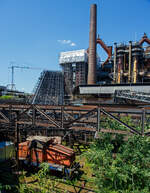 Die ex D V der AG der Dillinger Hüttenwerke (Normalspur – Diesellokomotive 5 /Henschel 29726), eine C-gekuppelte Henschel DH 440 Ca, hier am 01 Juli 2025 als Denkmal ausgestellt im Bereich der Kokssieberei der Völklinger Hütte. 

Die dreifachgekuppelte Lok vom Typ Henschel DH 440 Ca wurde 1959 von der Henschel-Werke GmbH in Kassel unter der Fabriknummer 29726 gebaut und als D V an die AG der Dillinger Hüttenwerke geliefert, wo sie bis 2000 im Dienst war. Die AG der Dillinger Hüttenwerke schenkte 2003 diese Lok dem Weltkulturerbe Völklinger Hütte, heutiger Eigentümer ist die Initiative Völklinger Hütte e.V., diese Lok war nie in Völklingen im Einsatz, aber ähnliche Lokomotiven dieser Bauart werden heute noch im Werksverkehr in Völklingen eingesetzt. Mit solchen Zügen wurden unter anderem Koks zur Kokssieberei transportiert, oder auch Schrottpakete zum Verladen in die Hängebahnwagen. Bei der AG der Dillinger Hüttenwerke sind baugleiche Loks im Werksverkehr in Dillingen im Einsatz. 

Übrigens die AG der Dillinger Hüttenwerke ist heute der einzige Produktionsstandort von Roheisen im Saarland und sie ist das größte Grobblechwerk Europas. Auch wenn die Saarstahl AG mit Anteilseigner ist, so darf man diese gleichsetzen. 

Zu den Loks:
Die Henschel DH 440 Ca sind C-gekuppelte standardisierte Werksbahn-Dieselloks der 3. Generation von Henschel mit dieselhydraulischem Antrieb mittels Kuppelstangen. Die 28 Lok von diesem Typ, mit einem mittelschnell laufenden MAN-Motor, wurden zwischen 1957 und 1965 gebaut. Allein 6 Exemplare wurden an die AG der Dillinger Hüttenwerke geliefert (D V bis D X).

Anders als die DH 440 der 2. Generation hat die DH 440 Ca (der 3. Generation) eine außenliegende Blindwelle (daher auch der Zusatz Ca), es ist auch größte Unterschied. Wobei auch einige Konstruktive Änderungen mitbrachte. 

TECHNISCHE DATEN:
Gebaute Anzahl: 28
Spurweite: 	1.435 mm (Normalspur)
Achsformel: C
Lokgewicht: ca. 43 t
Länge über Puffer: 8.900 mm
Fester Radstand: 3.000 mm
Kleinster bef. Halbmesser: 50 m
Höchstgeschwindigkeit:  30 km/h / 60 km/h
Motor: wassergekühlter 8-Zylinder 4-Takt MAN-Dieselmotor mit Aufladung vom Typ MAN W 8 V 17,5/22 A 
Hubraum: 42.320 ccm
Leistung: 324 kW (440 PS)
Nenndrehzahl: 1.100 U/min
Getriebe: Voith L 37 U
Leistungsübertragung: hydraulisch auf Blindwelle, von dieser über Kuppelstangen auf die Räder. 
